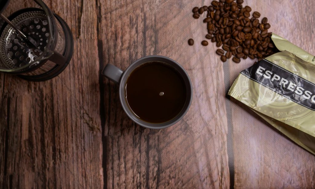 espresso in a cup next to a French press and scattered coffee beans spilling from a bag marked "espresso"