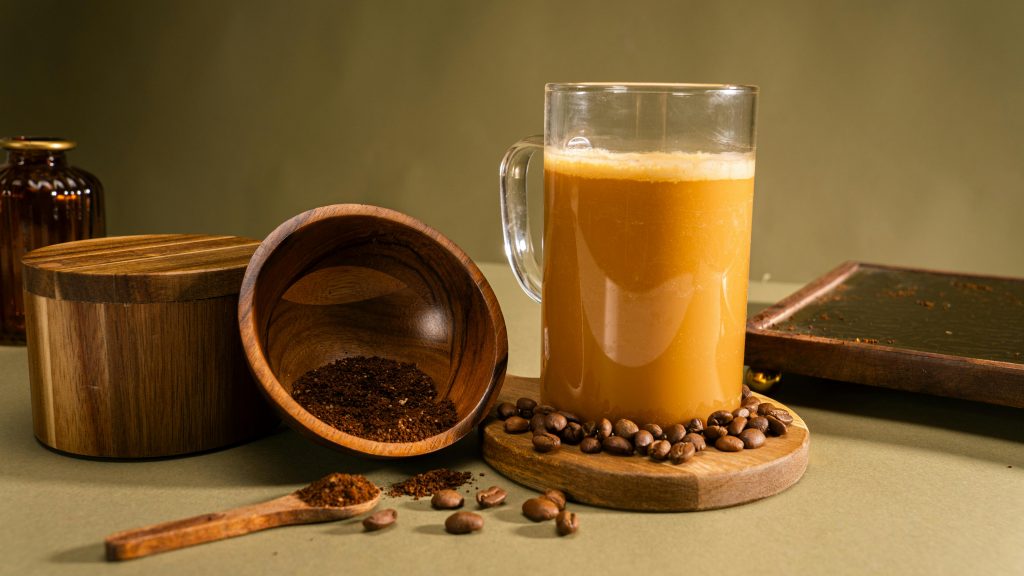coffee mug on a coaster next to a wooden bowl with ground coffee spilling onto the surface