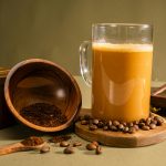 coffee mug on a coaster next to a wooden bowl with ground coffee spilling onto the surface