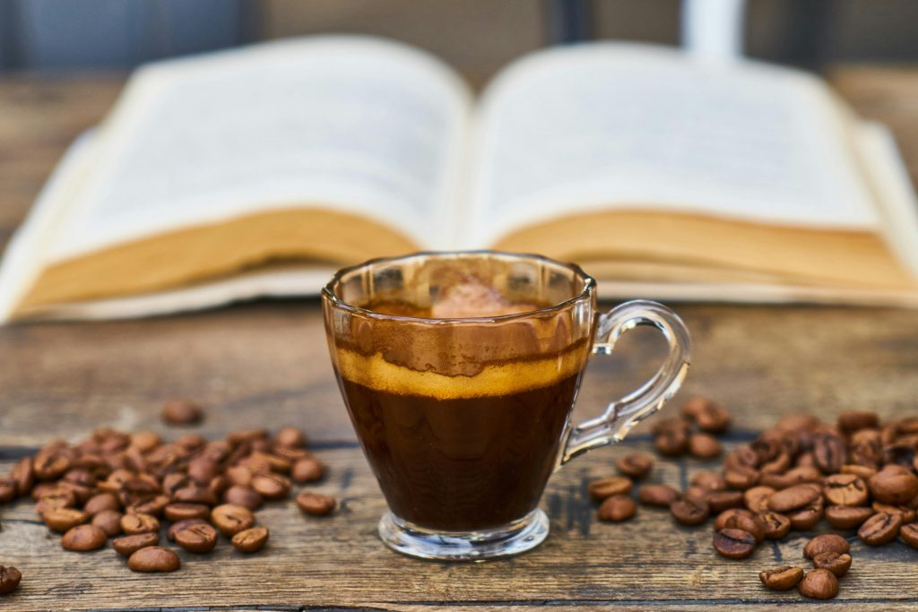 a cup of espresso with coffee beans and a book on a wooden table