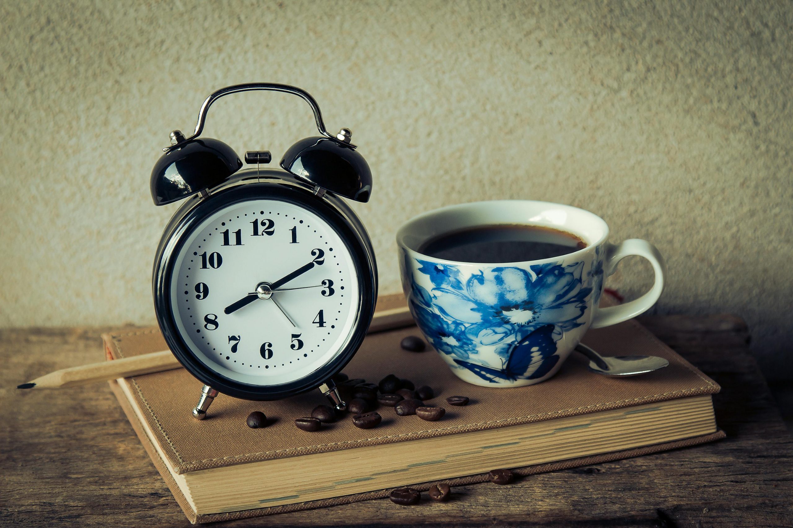 cup of coffee, alarm clock, and coffee beans on a book