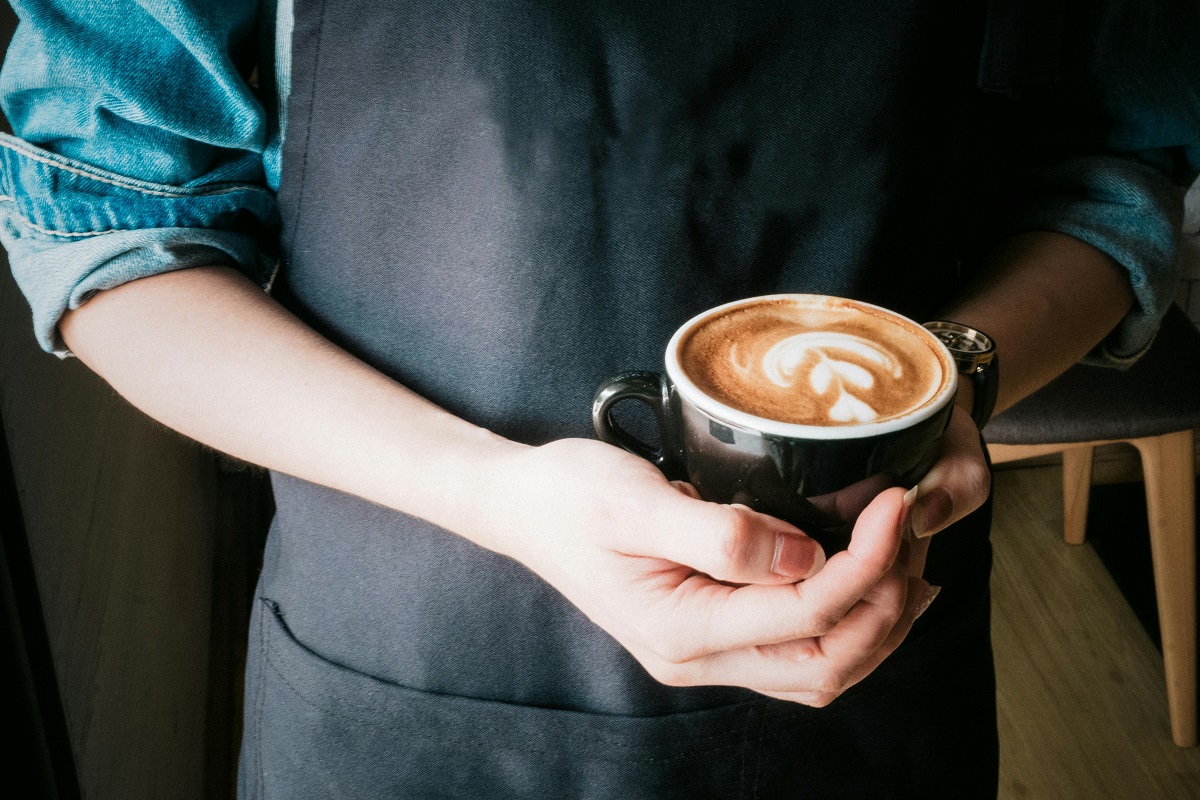 barista holding a cup of coffee with latte art