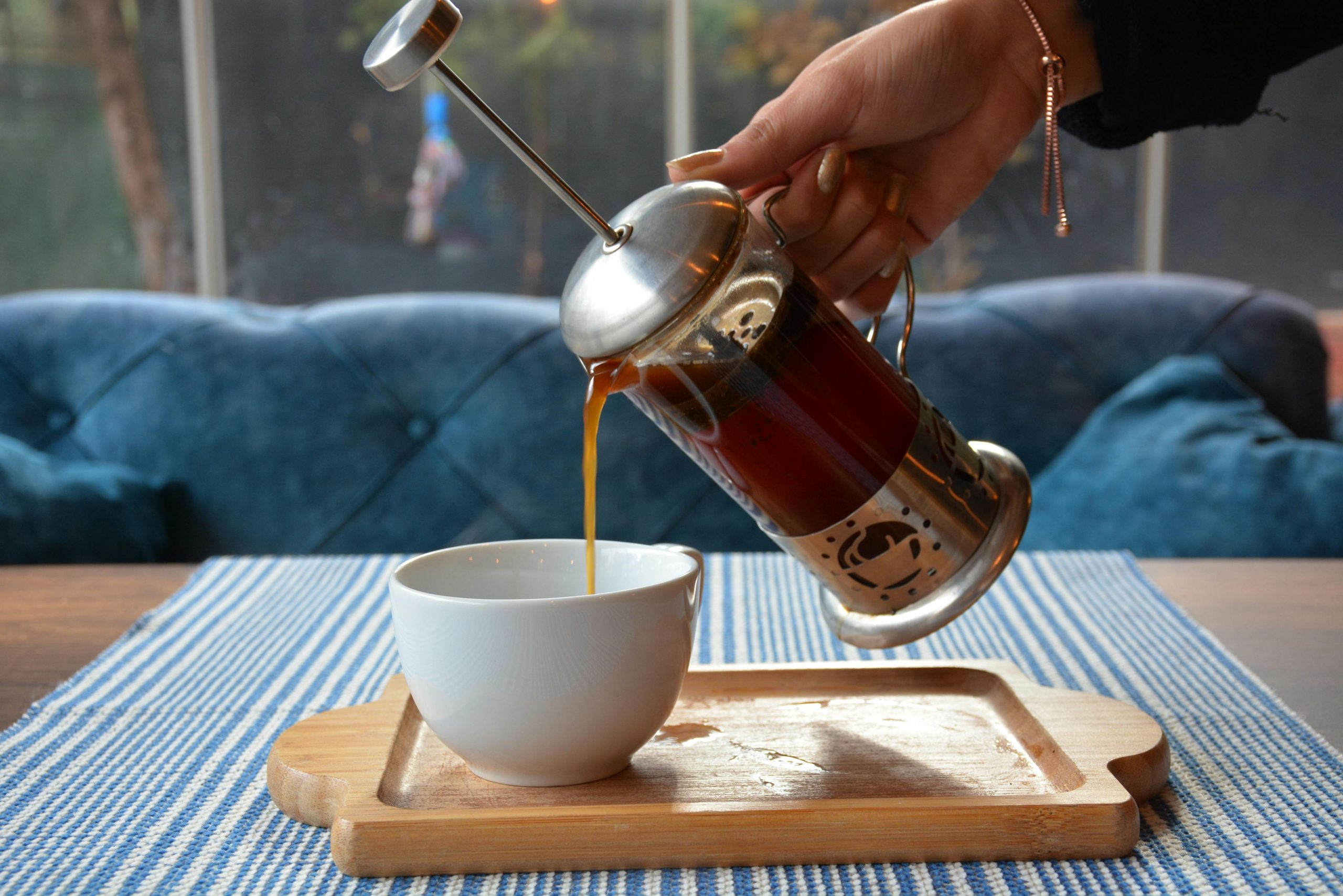 woman pouring french press coffee into a ceramic cup on a wooden tray