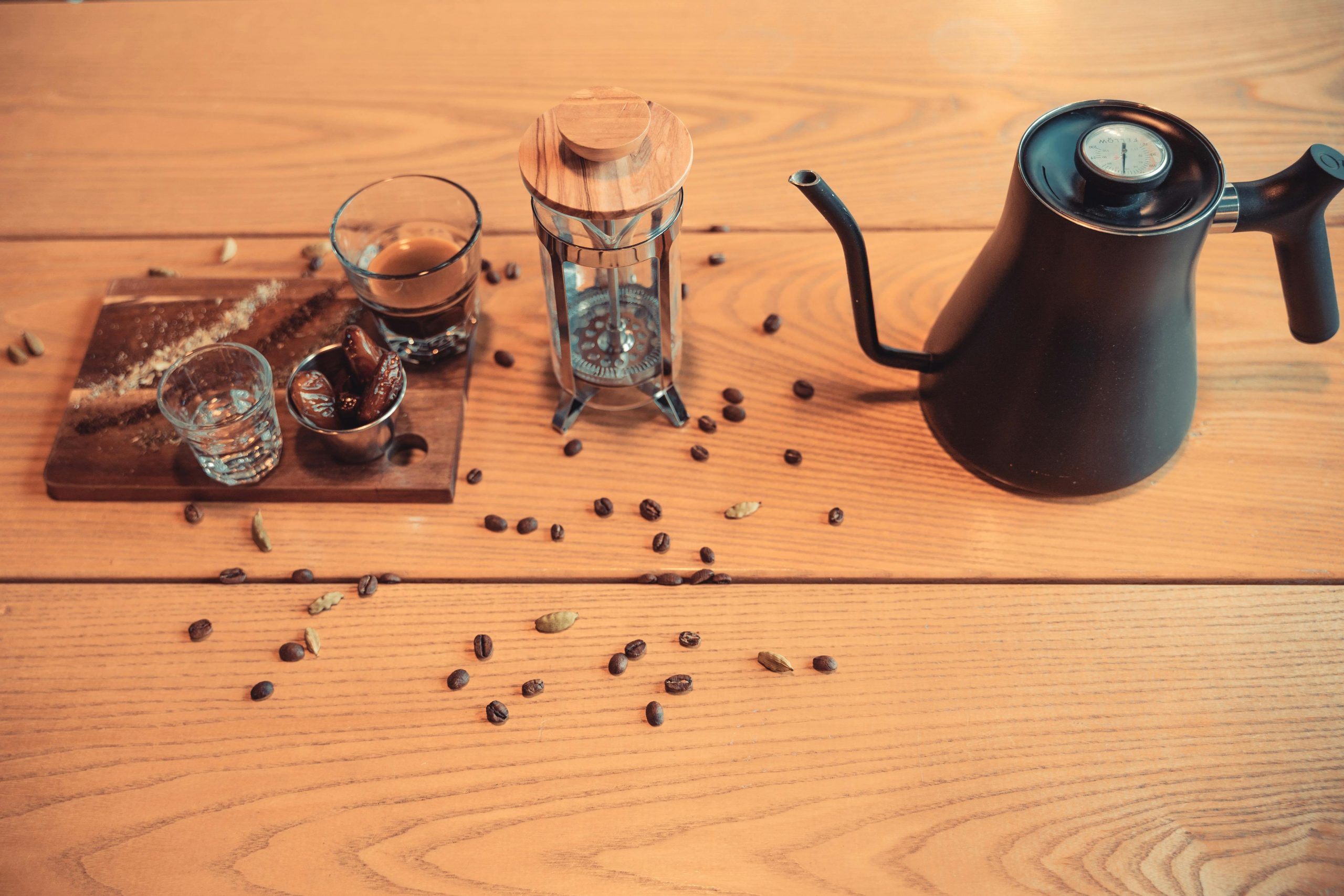 kettle, french press, shot glasses, and coffee beans on a wooden table