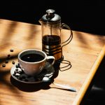french press and cup filled with coffee on wooden table