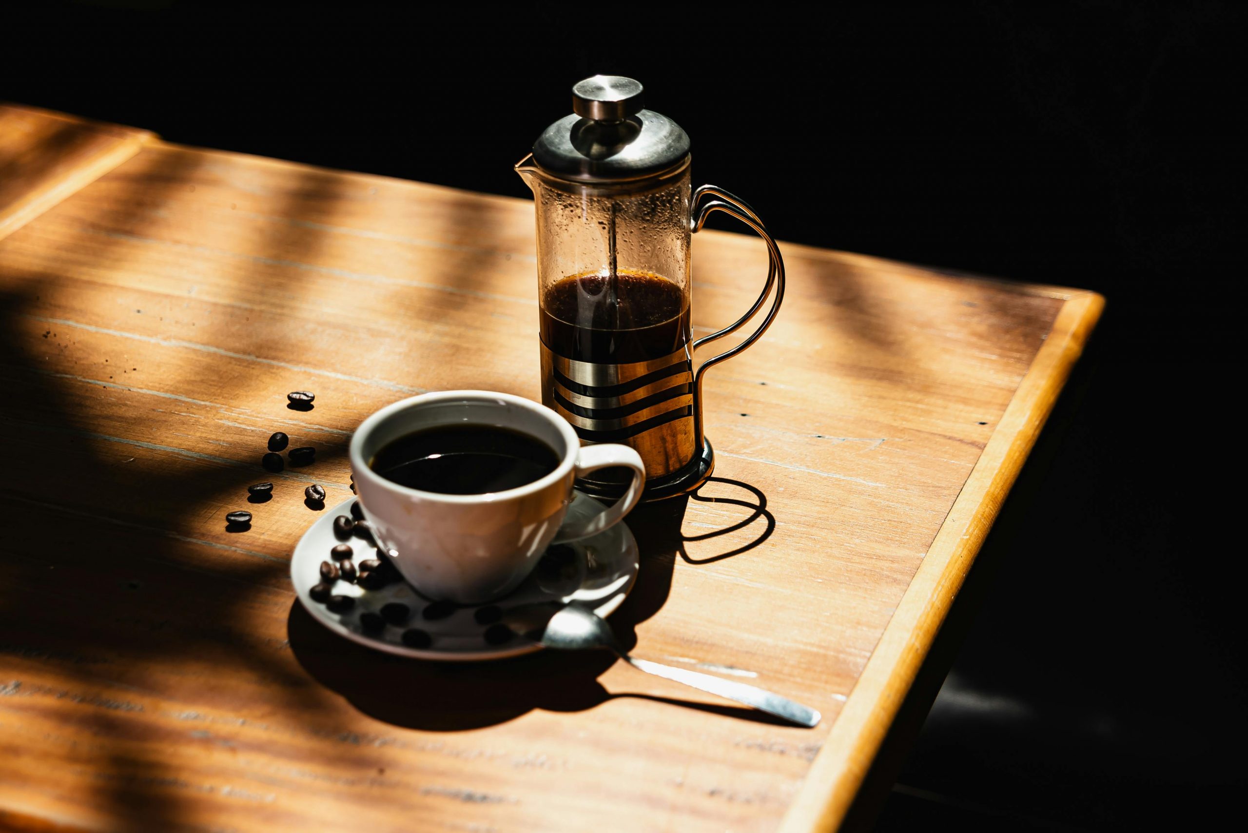 french press and cup filled with coffee on wooden table