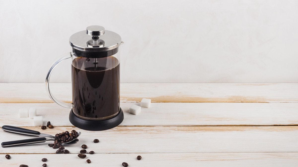 french press filled with coffee, coffee beans, and sugar cubes on a wooden table